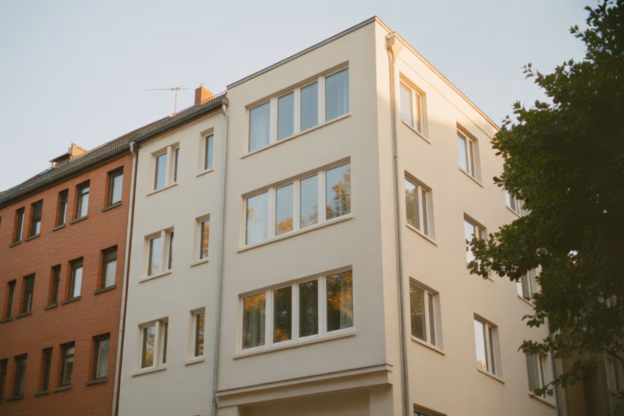 Mehrstöckiges Wohngebäude mit weißer, sauberer Fassade neben einem braunen Gebäude bei Sonnenlicht.