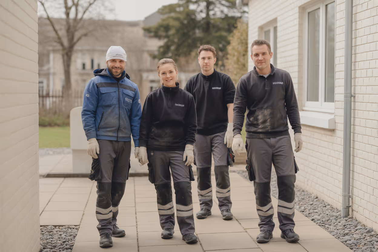 vier arbeitende in arbeitskleidung und handschuhen gehen auf einem gehweg zwisch